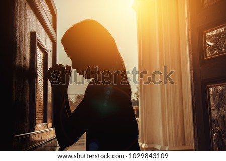 silhouette of woman kneeling and praying in modern church at sunset time Royalty-Free Stock Photo #1029843109