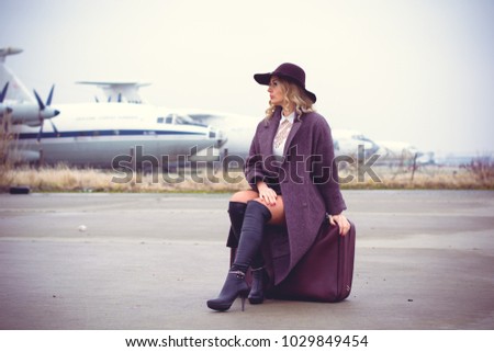 Nice blonde hair woman in the airport in vintage clothing and retro style. The concept of travel and recreation, the lady on suitcases going on the road