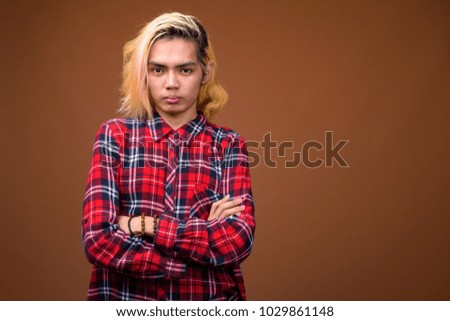 Studio shot of young Asian man wearing stylish clothes against brown background