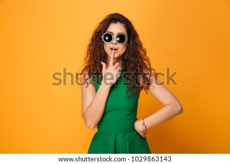 Picture of amazing young lady standing isolated over yellow background. Looking camera wearing sunglasses.
