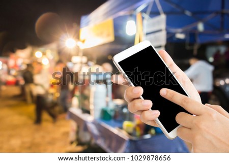 woman use mobile phone and blurred image of noodle shop on the street market in the country of Thailand