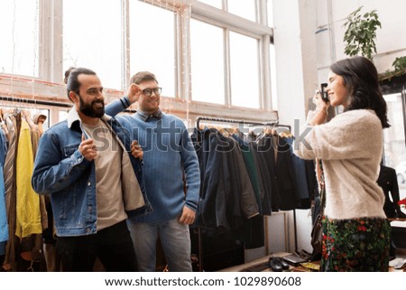 sale, shopping, fashion and people concept - friends choosing clothes and photographing by film camera at vintage clothing store