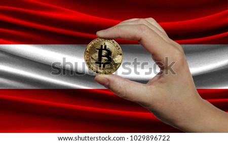 Hand of a man with a gold bitcone Cryptocurrency Digital bit of coins in a hand on a background of the flag of Austria.