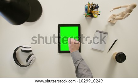 A finger zooming out on a tablet with a green screen. The tablet is on the white table. View from the top. Close-up.