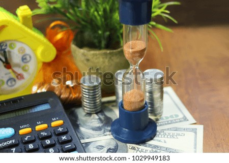 hourglass against the background hundred-dollar bills. columns of coins, a calculator, a clock in the form of a house, bags of coins, a plant in a clay pot. The concept of financial success