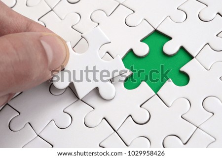 The human hand fills the last missing elements of the surface from the jigsaw puzzle. The concept of the completion of the initiated cases