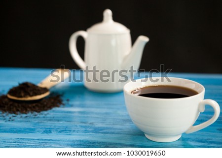 Hot tea next to a spoon with tea leaves on vintage blue board over black background