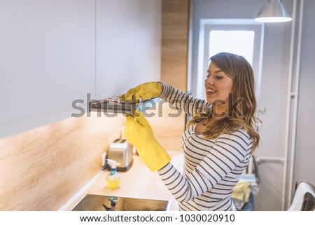Woman Cleaning Cooker Hood With Rag And Detergent In Kitchen. Close up of female hands in rubber protective yellow gloves cleaning the kitchen metal extractor hood with rag. Home, housekeeping concept