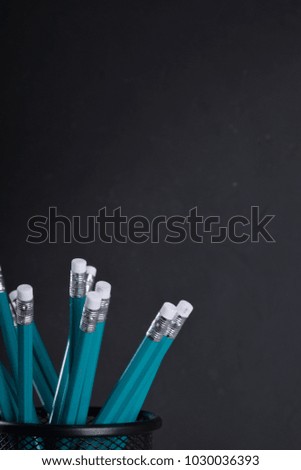 Pencils in metal holder pot in front of wall background
