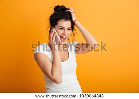 Image of happy young woman standing over yellow background wall. Looking aside talking by mobile phone.