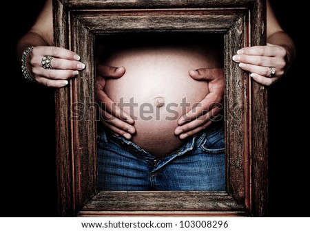 His hands embracing her Pregnancy with her hands holding a wooden frame embracing the moment