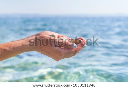Female hands with sea pebbles on the background of the sea.