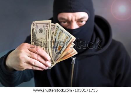 Thief in balaclava with dollars in hand. Corruption. Bribe. Fraud. Dark background