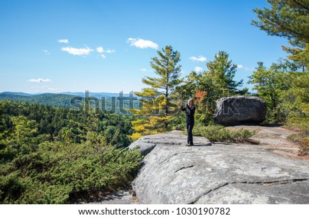 Woman taking a photo with her smart phone from the summit of Rattlesnake mountain in Willsboro NY