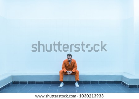 prisoner sitting on bench in prison room Royalty-Free Stock Photo #1030213933