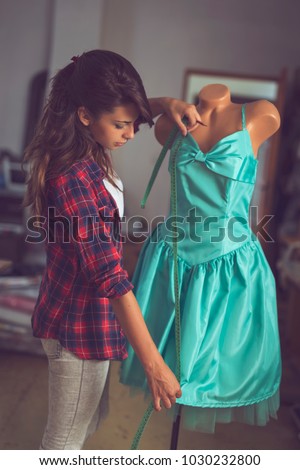 Young fashion designer working on a new dress in her atelier, taking measures with measuring tape
