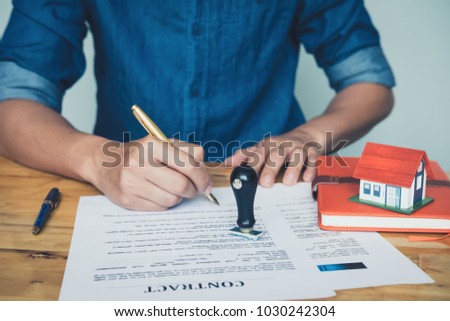 Rubber stamp put on the table between real estate agent holding house to his client after signing contract,concept for real estate,insurance with house, moving home or renting property