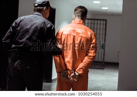 rear view of prison officer leading prisoner in handcuffs in corridor Royalty-Free Stock Photo #1030254055