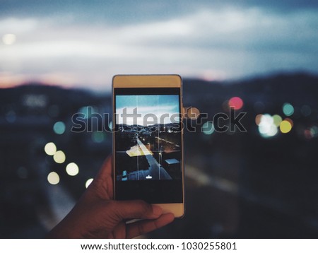 Woman hand holding smart phone for taking a picture city light view at night time.