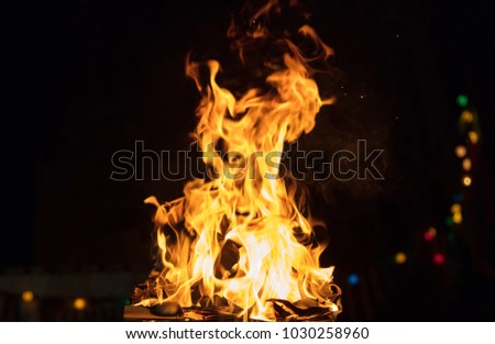 Fire in fireplace with firewood, colorful flames and bokeh lights. Big blaze on black blurred background. Close up view with details, space for text.