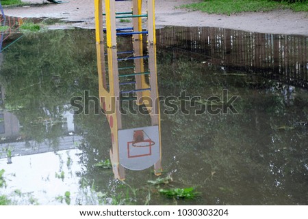 A large puddle on the children's playground. The basketball ring is reflected in the water. Sporty summer background 