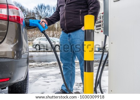 Man charging his electric car in the winter Royalty-Free Stock Photo #1030309918