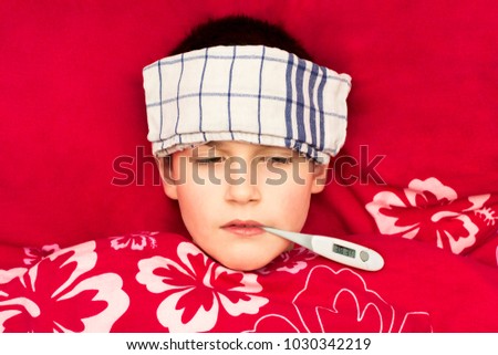A sick boy lying in bed with a thermometer in his mouth. Cold compress on the forehead of a child. Influenza epidemic in the Czech Republic. Temperature measurement in the mouth. Royalty-Free Stock Photo #1030342219