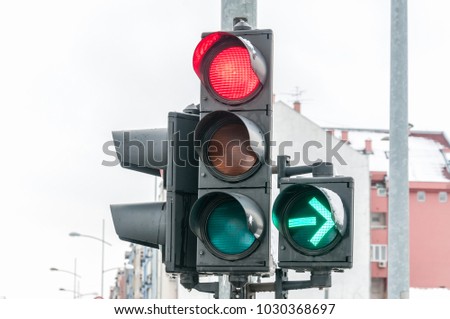 Close up of traffic light on the crossroad with red light for straight direction but green arrow for right turn only in the cold winter day with cloudy sky