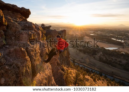 Adventurous man is rappeling down a cliff during a bright and vibrant sunny sunset. Taken in Smith Rock, Oregon, North America. Royalty-Free Stock Photo #1030373182