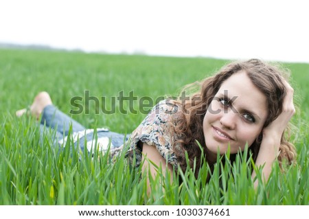 portrait of romantic, young woman with short hair lying on green grass (meadow, prairie) barefoot, dreams