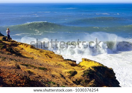 Coastal rocks over the ocean. A viewpoint on the edge of the cliff. Huge waves on the coast of Portugal. A man from the top takes pictures of the stormy ocean. The seaside resort of Nazare