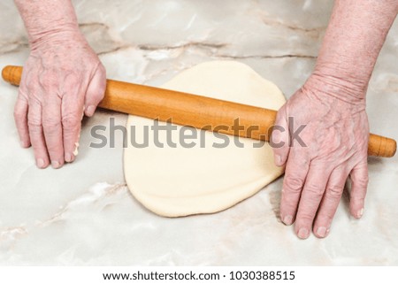 Hands of the old woman roll the dough on table