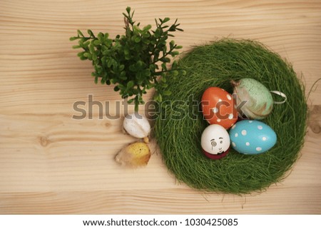 Colorful Easter eggs with green nest and pot of plant on a wooden background 