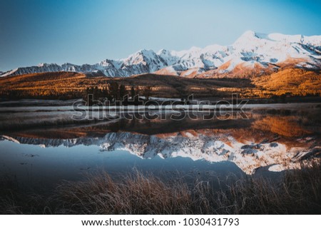 Mirror surface of the lake in the mountain valley. The peaks of the cliffs on the horizon at the colorful sky. Autumn weather