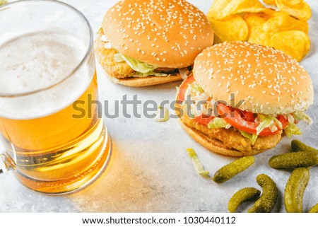 Chicken burger and glass of beer. Homemade hamburgers, pickles and chips  on wooden tray. White marble background. 