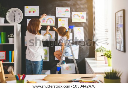 Mother and child girl hang their drawings on the wall