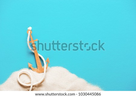 Blue background with handmade paper anchor on the sand, copy space 