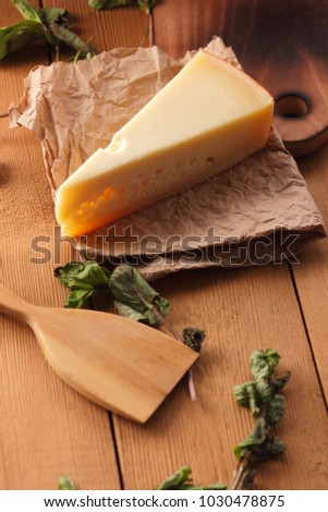 Hard cheese, lemon, lime and mint on a wooden background, wooden spatula, mint leaves with cheese and holes, rustic style, parchment cheese, healthy food, art