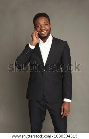 Happy young black man portrait in formal wear talking on smartphone at grey studio background, crop