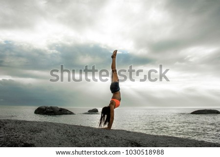 Woman doing a handstand on a rock at sunset on Bakovern Beach, Cape Town. 
