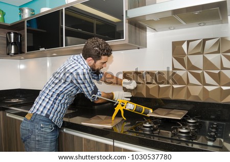 Man renovating, renovating the kitchen, installing tile on the wall. Royalty-Free Stock Photo #1030537780