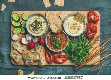 Vegan snack board. Flat-lay of Various Vegetarian dips hummus, babaganush and muhammara with crackers, bread, fresh vegetables on wooden board over grey background. Clean eating, dieting food concept Royalty-Free Stock Photo #1030537957