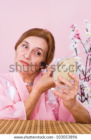 Happy Caucasian aged woman sitting at a table on a pink background