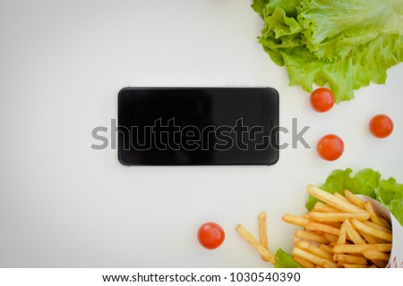 Mobile phone, fresh salad, fries and cherry tomatos delicious appetizing top view light table background. Blank screen mock up display gourmet nutrition picture. Ready healthy diet design photo