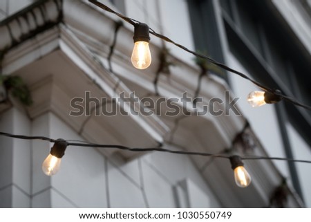 White incandescent strand lights hanging outside of a restaurant, with a white marble archway in the blurry background