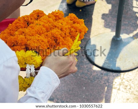 Woman in white shirt making merit and praying at temple, tray of marigold garland and candle  holding in hand, have space background