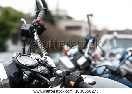 Close up on the chrome speed gauge and handle bars of a vintage motorcycle, with a row of parked bikes in the blurry background