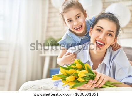 Happy women's day! Child daughter is congratulating mom and giving her flowers tulips. Mum and girl smiling and hugging. Family holiday and togetherness.