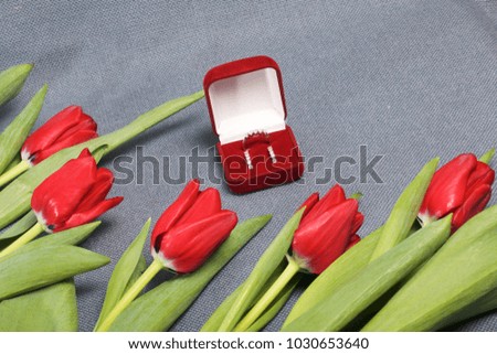 Gifts for loved ones. A bouquet of red tulips. Nearby is a red velvet box with a ring and earrings.
