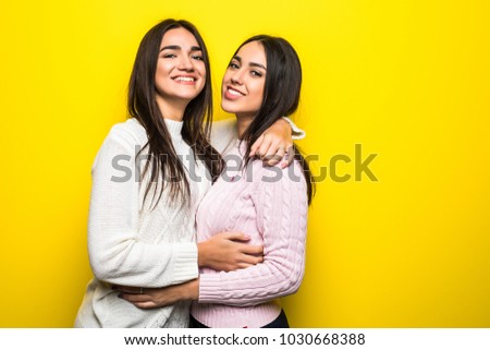 Portrait of two happy girls dressed in sweaters hugging isolated over yellow